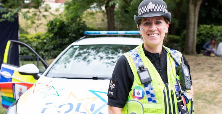 Police woman in front of police car smiling at camera