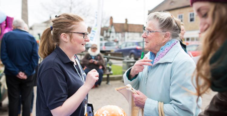 A female volunteer talking to an elderly lady at a community event.