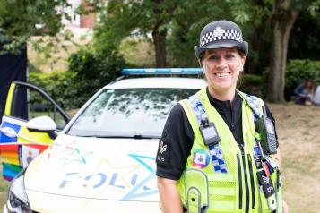 Police woman in front of police car smiling at camera