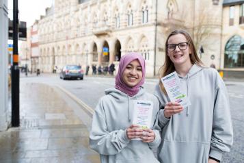 Two young female volunteers holding Healthwatch leaflets