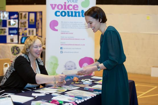 Volunteer handing over a leaflet to woman at a stall